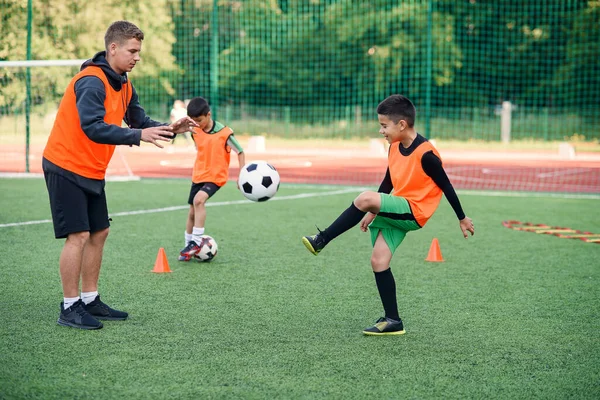 Mladý fotbalový trenér učí teenagery. Mladý profesionální trenér trénuje míč kopy s mladými fotbalisty. — Stock fotografie