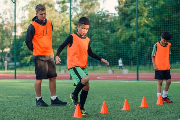 Gemotiveerde sportieve dertigers in oranje vesten tussen de plastic kegels tijdens voetbaltraining in het stadion. — Stockfoto