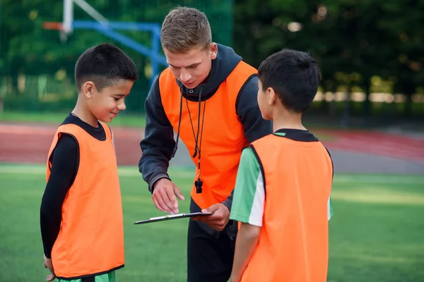 足球教练教青少年足球运动员.年轻的职业教练向孩子们解释比赛的策略. — 图库照片
