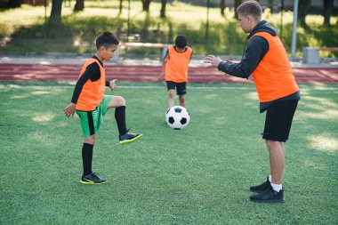 İki okul çocuğu futbol yaz kampında koçla sıkı bir futbol antrenmanı yapıyor..
