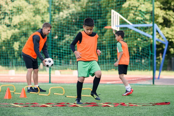 Due ragazzi della scuola stanno conducendo delle esercitazioni a scala sul prato durante il campo estivo di calcio. Intenso allenamento di calcio con allenatore. — Foto Stock