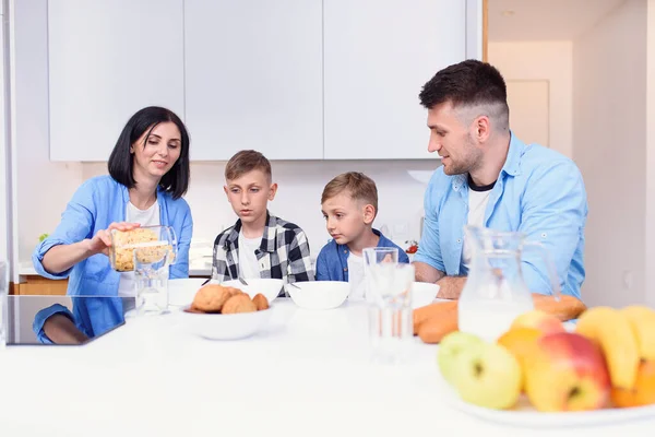 Happy family with two sons eating healthy morning breakfast at modern cozy kitchen at dining table.