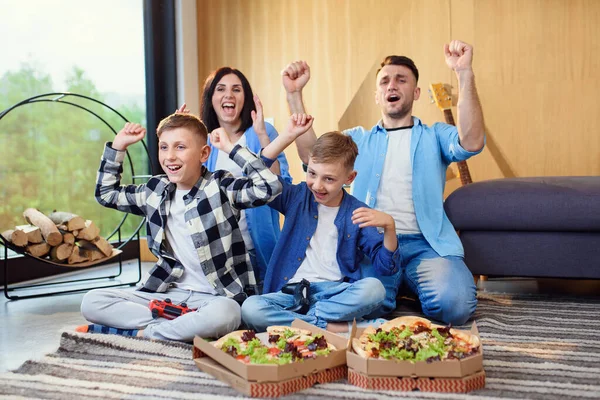 Família moderna feliz se divertir jogando jogos de vídeo com gamepads e comer pizza saborosa. — Fotografia de Stock