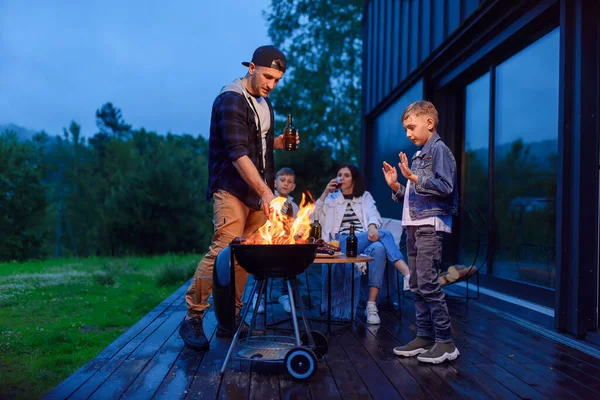 Glücklicher Vater und Sohn beim Grillen im Familienurlaub auf der Terrasse ihres modernen Hauses am Abend. — Stockfoto