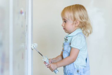 Yeni yürümeye başlayan komik kız yeni bir dairede duvarı beyaz boya silindiriyle boyuyor. Aile onarım dairesi.