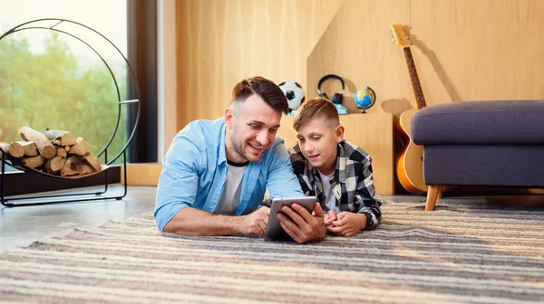 Niño con el padre acostado en el suelo usando tableta PC en el apartamento moderno. Feliz tiempo en familia juntos. — Foto de Stock