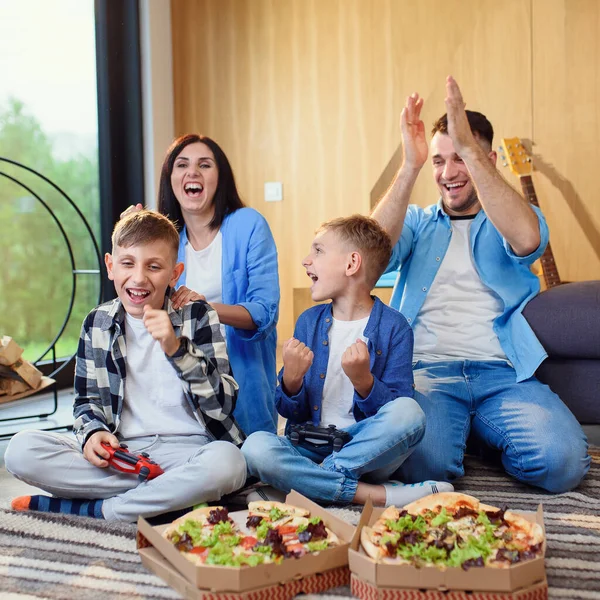 Família moderna feliz se divertir jogando jogos de vídeo com gamepads e comer pizza saborosa. — Fotografia de Stock