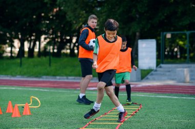Profesyonel futbol antrenörü, futbol sahasındaki engelleri aşarak öğrencilerinin koşu egzersizleri yapmasını izliyor.