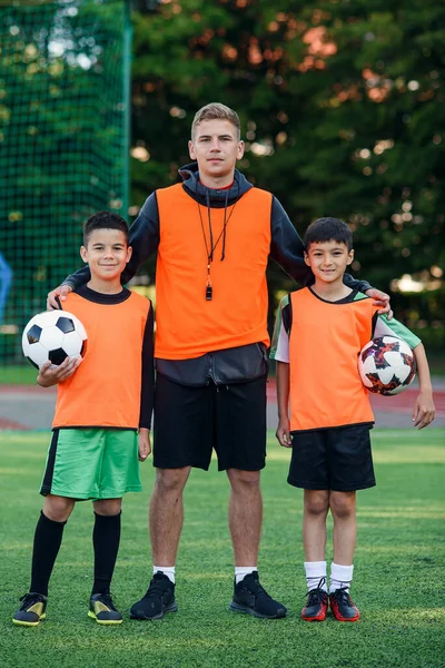 Happy teen jogadores de futebol em pé no campo de futebol verde com o treinador e olhando para a câmera com sorrisos. — Fotografia de Stock