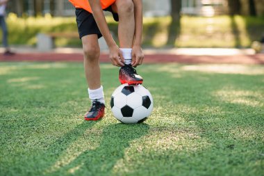 Futbolcunun bacağını topa bağlayan ve futbol stadyumunda ayakkabı bağı bağlayan çizmesini kapat..