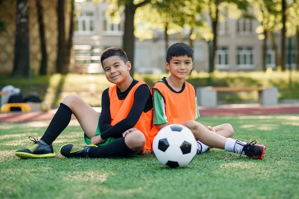 Bonito alegre adolescente jogadores de futebol descansando sobre a cobertura de grama artificial do campo de futebol após o treinamento. — Fotografia de Stock