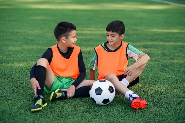 Bonito alegre adolescente jogadores de futebol descansando sobre a cobertura de grama artificial do campo de futebol após o treinamento. — Fotografia de Stock