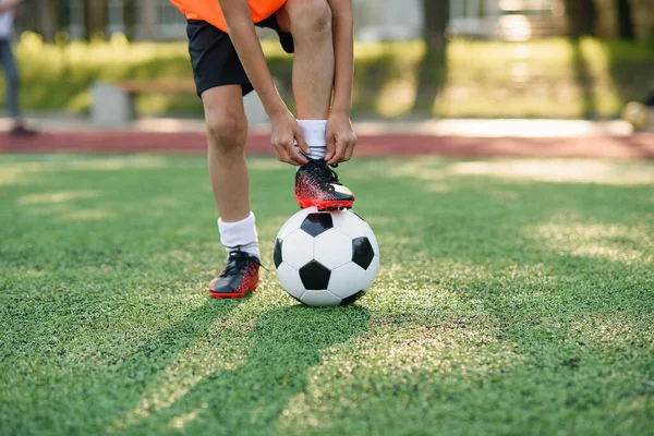 足球运动员的近身靴，将他的腿放在球上，并在训练中把鞋带绑在足球场上. — 图库照片