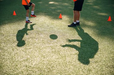 Futbol antrenmanı konsepti. Futbol koçunun çimlerindeki gölgeler genç futbolcularla top tekmeleri öğretir..