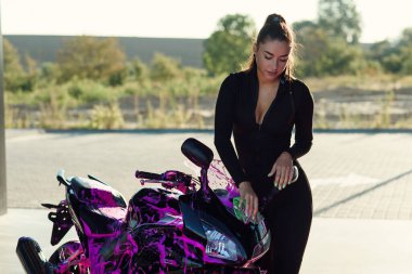 Dar ve baştan çıkarıcı takım elbiseli güzel bir kız şık bir spor motosikleti yıkar ve güneş doğarken onu mor köpükten siler..