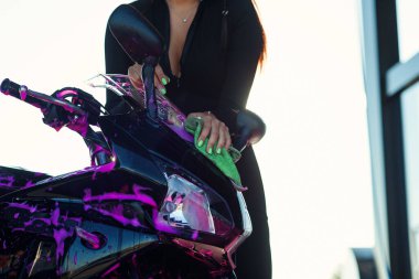 Dar takım elbiseli baştan çıkarıcı kız şık bir spor motosikleti yıkıyor ve güneş doğarken onu mor köpükten temizliyor..