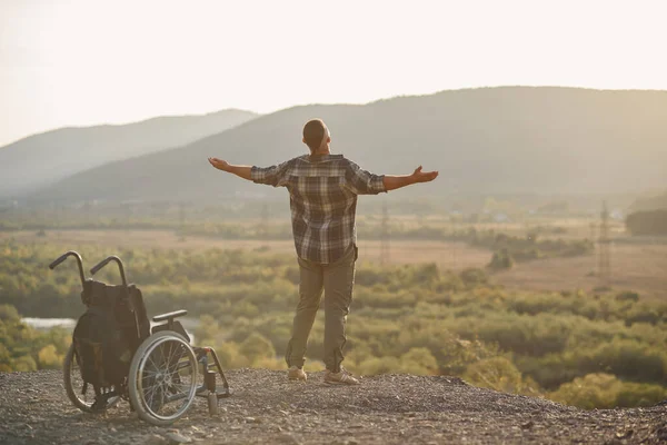Молодий чоловік піднявся на ноги з інвалідного візка на вершині гори на сході сонця. Некоректність була зцілена . — стокове фото