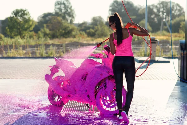 Menina deslumbrante bonita lava uma motocicleta em auto-serviço carwash com jato de espuma de alta pressão. — Fotografia de Stock