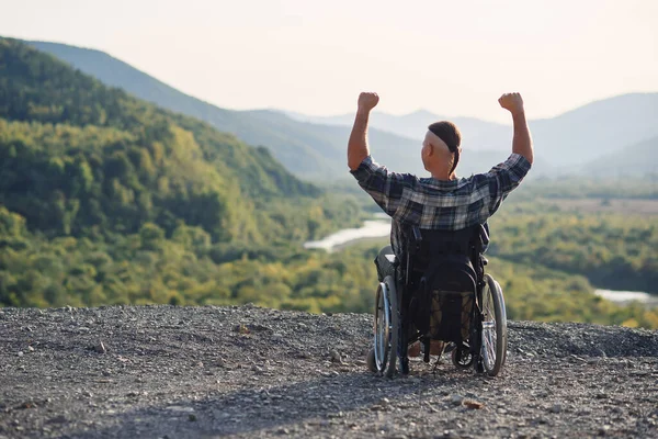 Самотній молодий чоловік у інвалідному візку насолоджується свіжим повітрям у сонячний день на горі. Люди з інвалідністю подорожують . — стокове фото