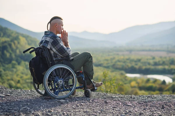 Молодий чоловік у інвалідному візку насолоджується красою природи в горах. Реабілітація після травми . — стокове фото