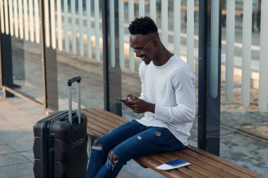 Sırt çantası ve akıllı telefonlu genç sakallı turist şehir merkezinde durup tramvayda bekliyor..