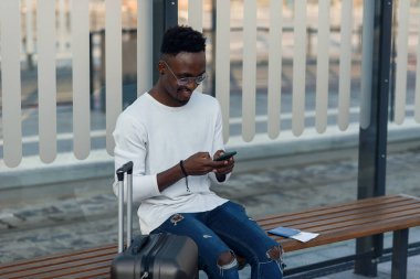 Sırt çantası ve akıllı telefonlu genç sakallı turist şehir merkezinde durup tramvayda bekliyor..