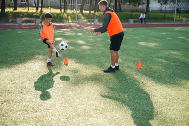 Genç futbol koçu genç oyuncuları eğitir. Genç bir profesyonel koç genç futbolcularla topa vurmayı öğretir..