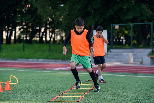 Due ragazzi della scuola stanno conducendo delle esercitazioni a scala sul prato durante il campo estivo di calcio. Intenso allenamento di calcio con allenatore. — Foto Stock