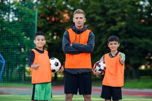 Happy teen jogadores de futebol em pé no campo de futebol verde com o treinador e olhando para a câmera com sorrisos. — Fotografia de Stock