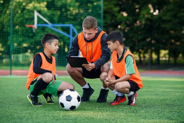 Professional soccer coach tells the strategy of football game to his attentive teen players at stadium during training.