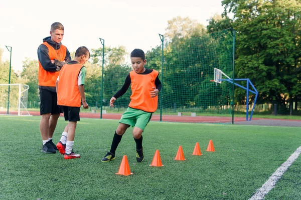 Gemotiveerde tiener voetbalspelers uitvoeren run oefeningen met het overwinnen van obstakels van toepassing rekken op kunstmatige voetbalveld. — Stockfoto