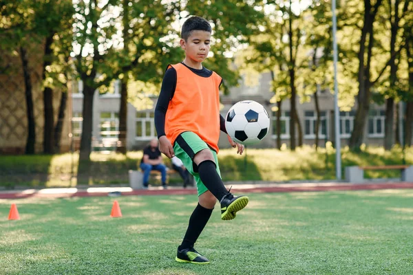 Motivovaný mladý fotbalista nacpe fotbalový míček do bot. Cvičení sportovních cvičení na umělém stadionu. — Stock fotografie