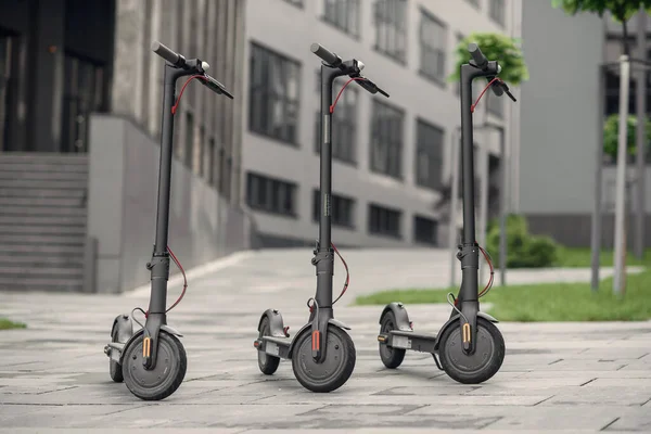 Tres modernos y elegantes scooter eléctrico negro están aparcados cerca del gran centro de oficinas. Electricidad y concepto ecológico. — Foto de Stock
