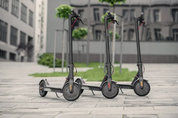 Tres modernos y elegantes scooter eléctrico negro están aparcados cerca del gran centro de oficinas. Electricidad y concepto ecológico. — Foto de Stock