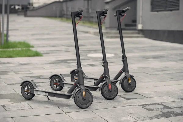 Three modern stylish black electric scooter are parked near big office centre. Electricity and eco friendly concept. — Stock Photo, Image