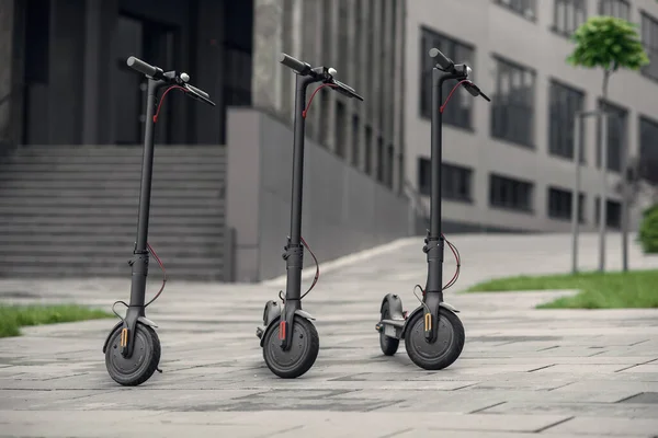 Три современных стильных черных электрических скутера припаркованы рядом с большим офисным центром. Электричество и экологическая концепция. — стоковое фото