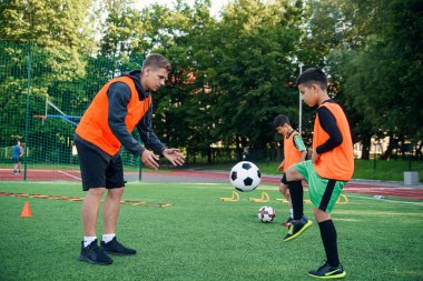 Futbol formalı yetenekli bir genç oyuncu spor sahasında tecrübeli koçuyla topa vuruyor.