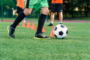Spor giyiminde ısrarcı genç çocuk futbol sahasında futbol antrenmanı yapıyor ve antrenman konileri arasında dönüp durmayı öğreniyor..