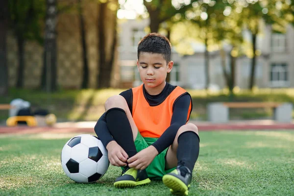 Cansado adolescente jogador de futebol ao ar livre estádio de esportes artificiais e amarrar o cadarço em suas botas de treinamento. — Fotografia de Stock