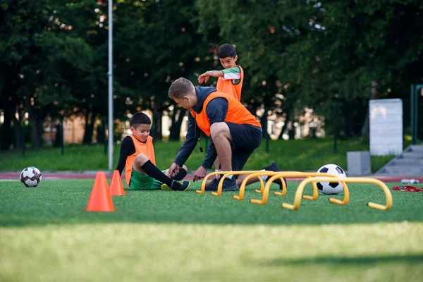 Teen soccer player injured his leg during training. Kids injury in sport concept. Coach help his pupil after accident. — Stock Photo, Image
