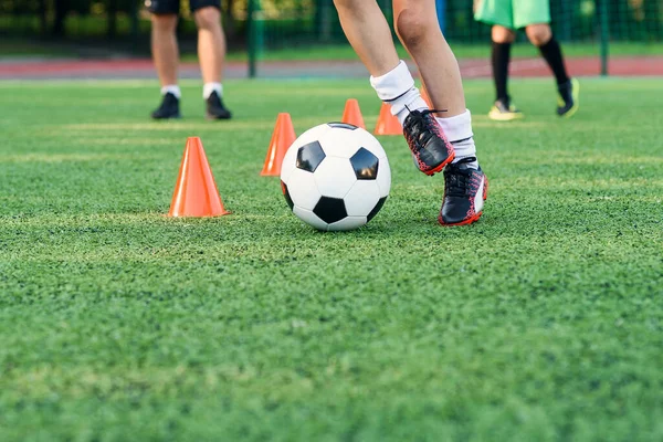 Close up boy in abbigliamento sportivo allena il calcio sul campo di calcio e impara a girare la palla tra i coni arancioni di formazione. — Foto Stock