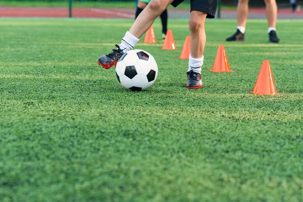 Adolescente persistente in abbigliamento sportivo allena il calcio sul campo di calcio e impara a cerchio la palla tra i coni di allenamento. — Foto Stock