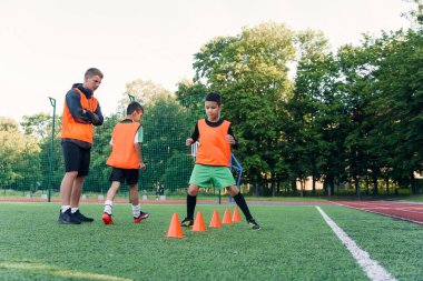Stadyumdaki futbol antrenmanlarında plastikler arasında koşan turuncu üniformalı genç sporcu çocuklar..