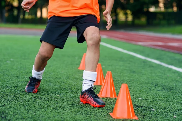 Zblízka fotbalisté nohy běží mezi plastové oranžové kužely na stadionu během profesionálního tréninku. — Stock fotografie