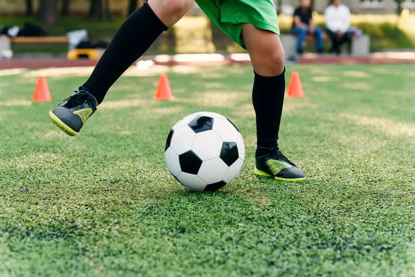 Jovem jogador de futebol persistente chutando bola no campo. Fechar os pés de futebol chutando bola na grama verde. — Fotografia de Stock