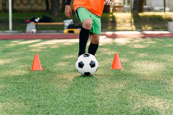 Hartnäckiger Teenager-Fußballer, der Ball auf dem Feld kickt. Füße eines Fußballers, der Ball auf grünem Rasen kickt, aus nächster Nähe. — Stockfoto