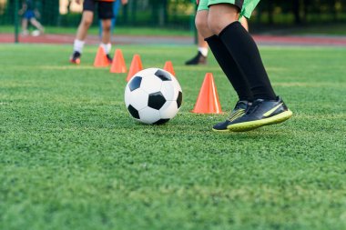 Spor giyiminde ısrarcı genç çocuk futbol sahasında futbol antrenmanı yapıyor ve antrenman konileri arasında dönüp durmayı öğreniyor..
