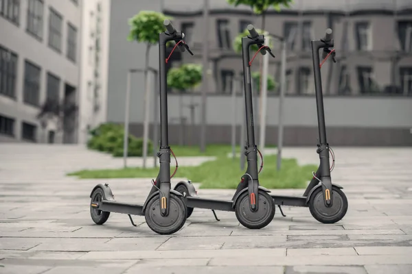 Три современных стильных черных электрических скутера припаркованы рядом с большим офисным центром. Электричество и экологическая концепция. — стоковое фото
