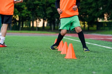 Spor yaparken yapay stadyumun üzerinde duran plastik turuncu koniler arasında koşan futbolcuların bacaklarını kapat..