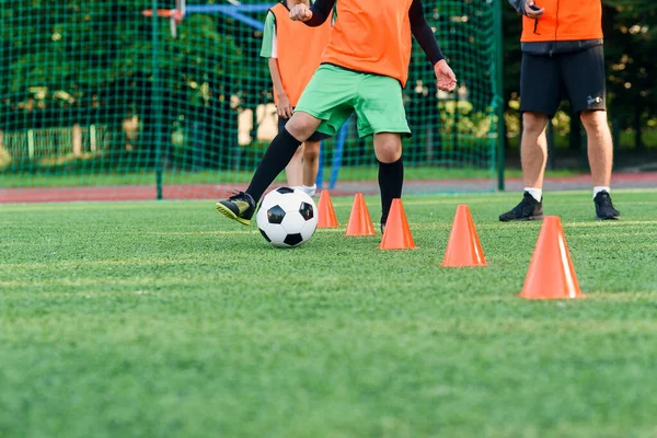 Закрыть подростка в спортивной форме тренирует футбол на стадионе и учится кружить мяч между тренировками оранжевые конусы. — стоковое фото